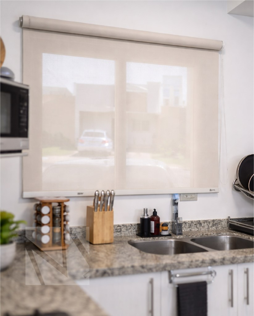 Cocina moderna minimalista con encimera de granito, fregadero doble de acero inoxidable y luz natural entrando por ventana con cortina roller.