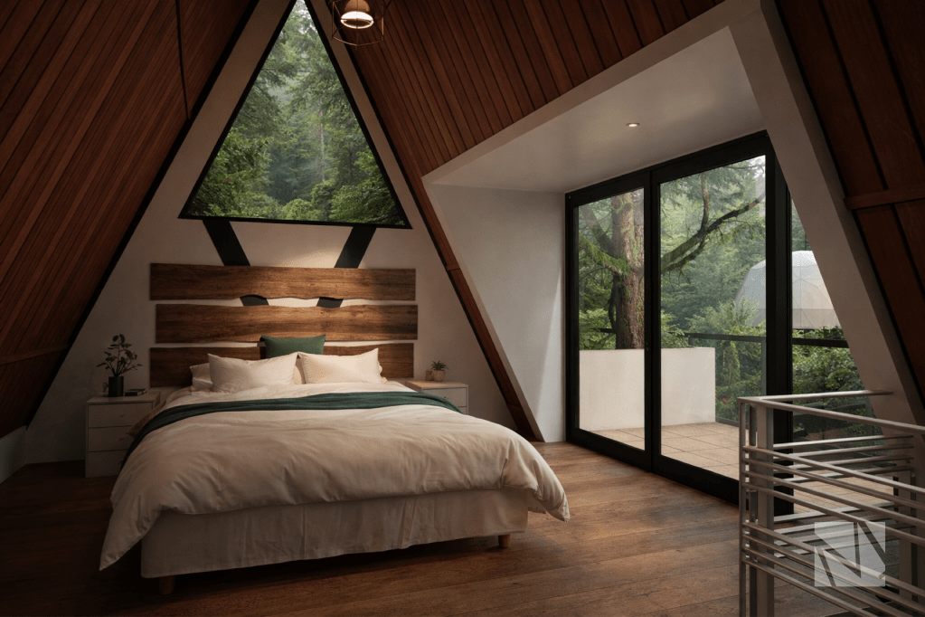 Dormitorio en cabaña tipo A-frame con ventana triangular y vista al bosque.