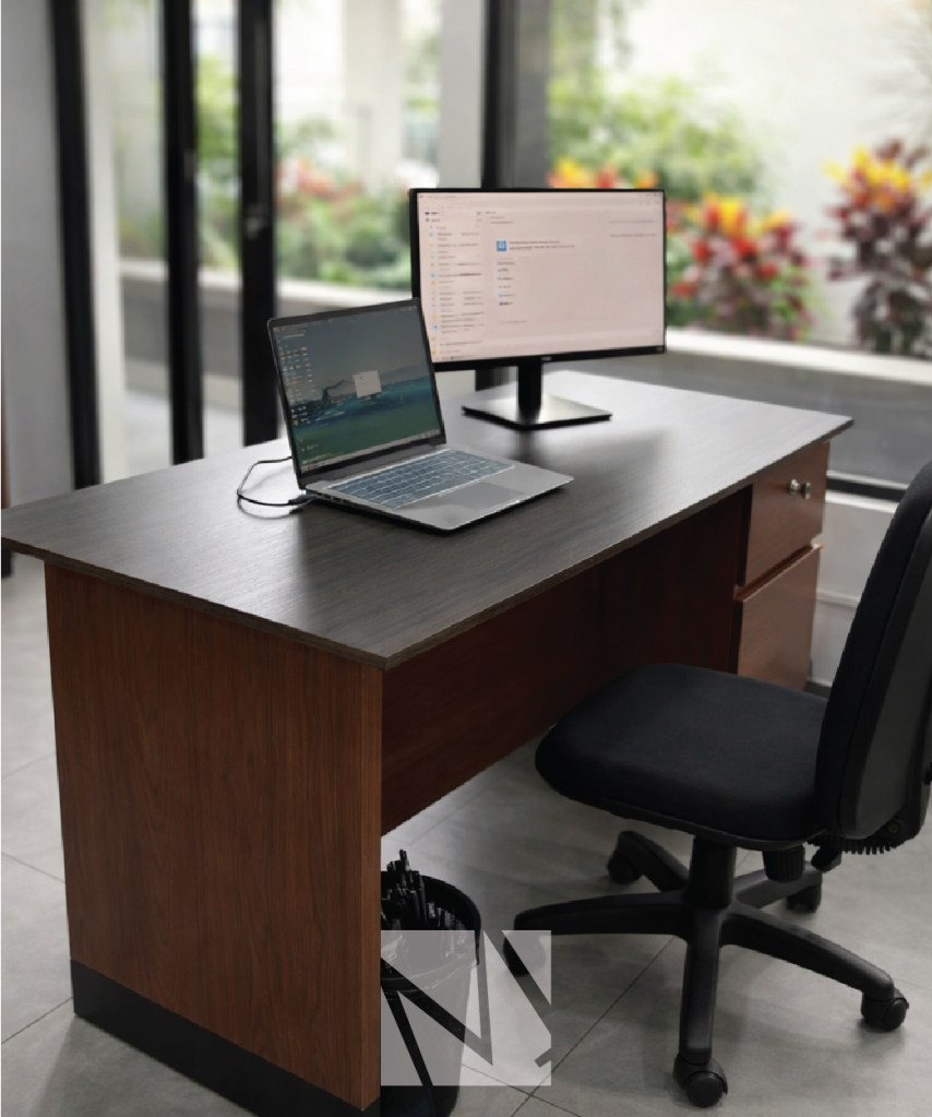 Escritorio de oficina moderno con acabado en madera y superficie oscura, acompañado de silla ergonómica y estación de trabajo, representando soluciones de mobiliario corporativo de Modulare